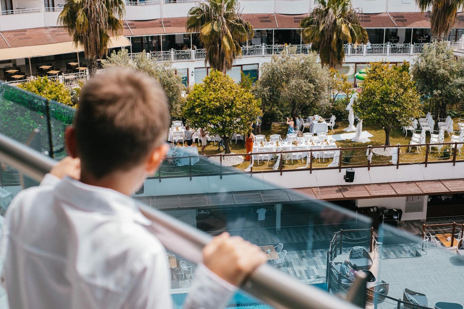 Skats no Castival Hotel balkona uz svētku pasākumu dārzā un baseina zonu — viesnīcas iekšpagalms ar palmām un dekorācijām