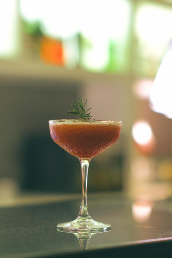 Castival Hotel bāra piedāvājums — elegants kokteilis stikla glāzē ar rozmarīna dekoru uz tumšas letes fona