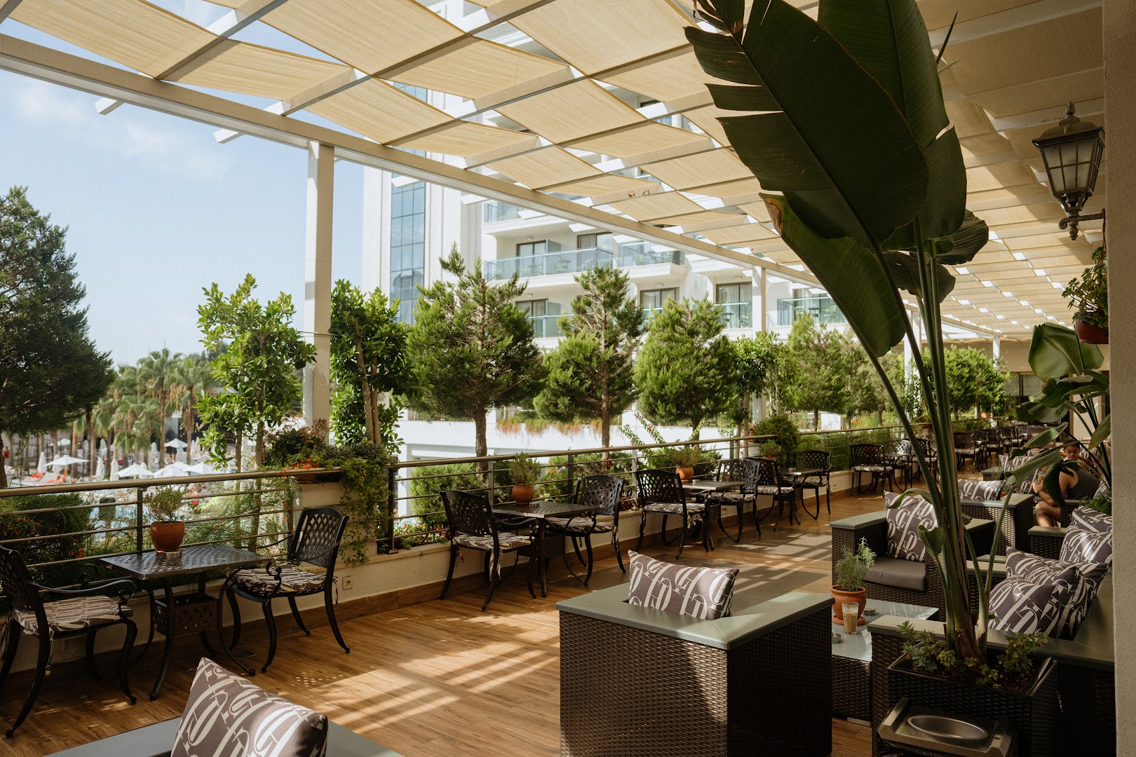 Castival Hotel plašā āra atpūtas zona ar dīvāniem un galdiņiem uz koka terases, skats uz viesnīcas ēku un dārzu