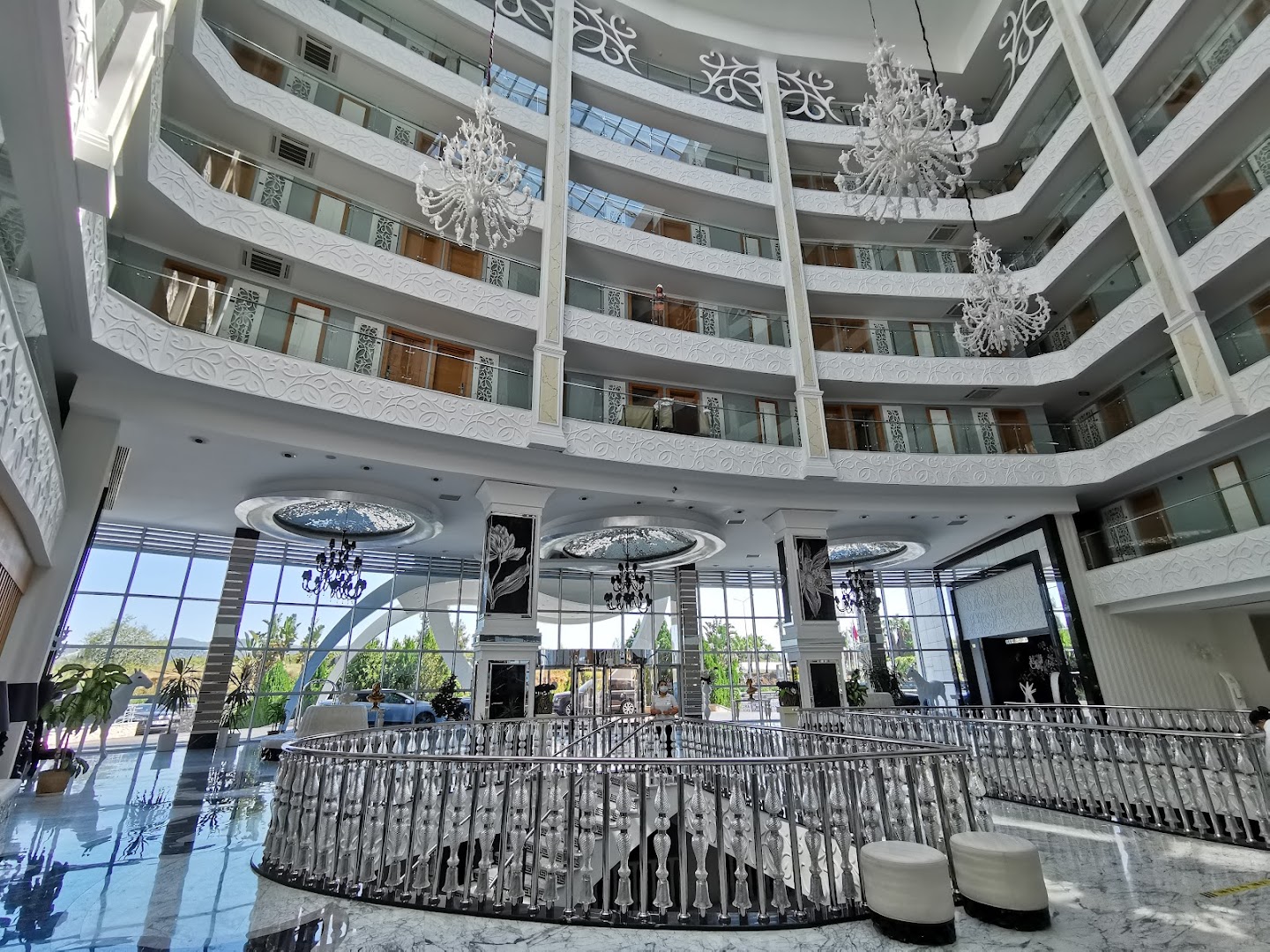 Q Premium Resort Hotel iespaidīgais vestibils ar vairākiem stāviem, greznām lustrām un stikla liftiem Alānijā — plašs un gaišs interjers