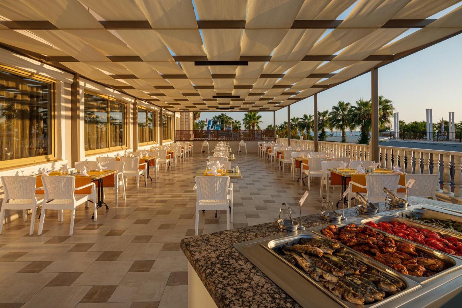Aydinbey Famous Resort restorāna āra terase ar klātiem galdiem, bufetes zonu un tentu aizsegu pret sauli