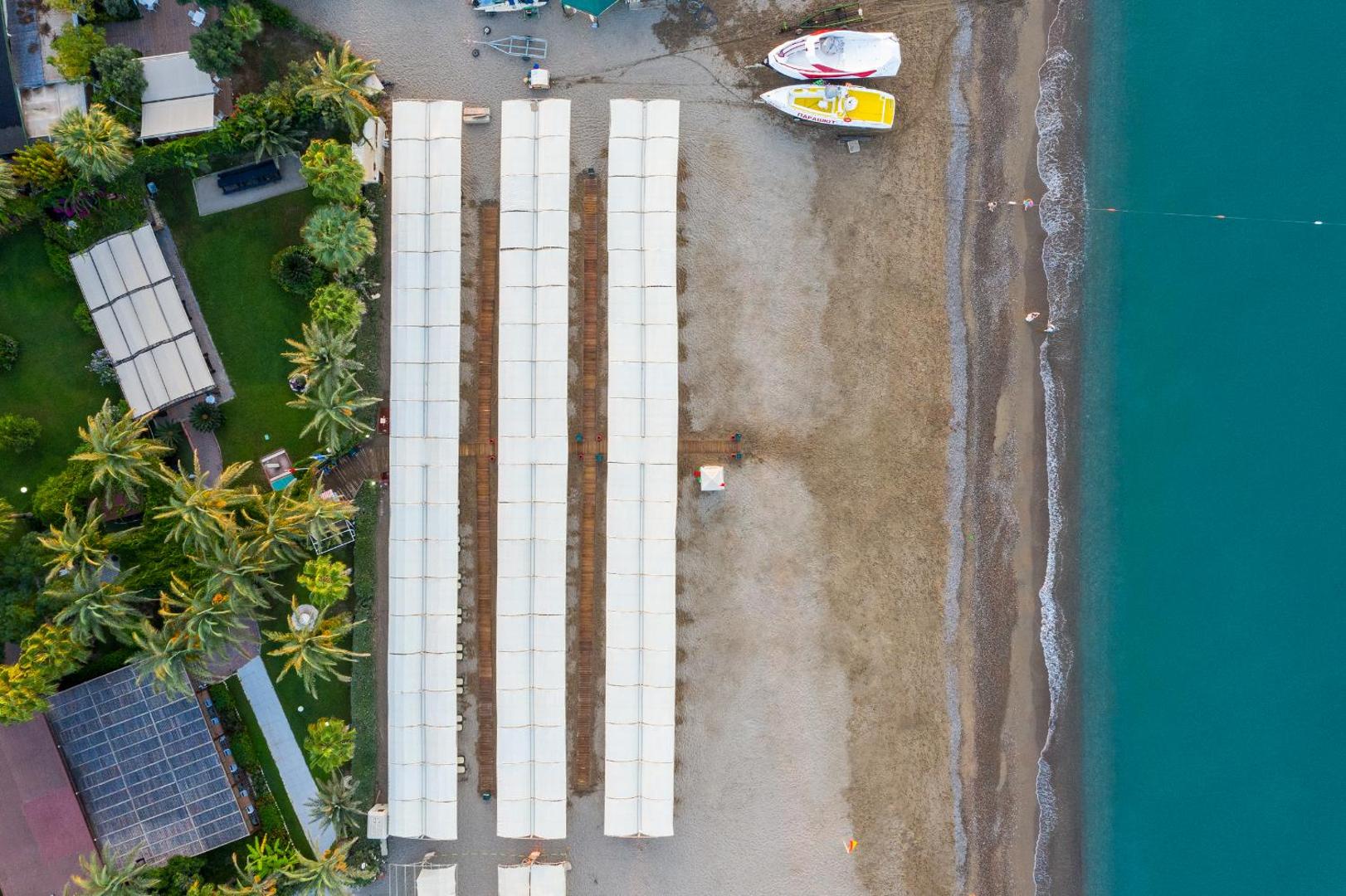 Aydinbey Famous Resort privātā pludmale no augšas — saulessargu rindas, smilšu krasts un tirkīzzila jūra Belekas reģionā