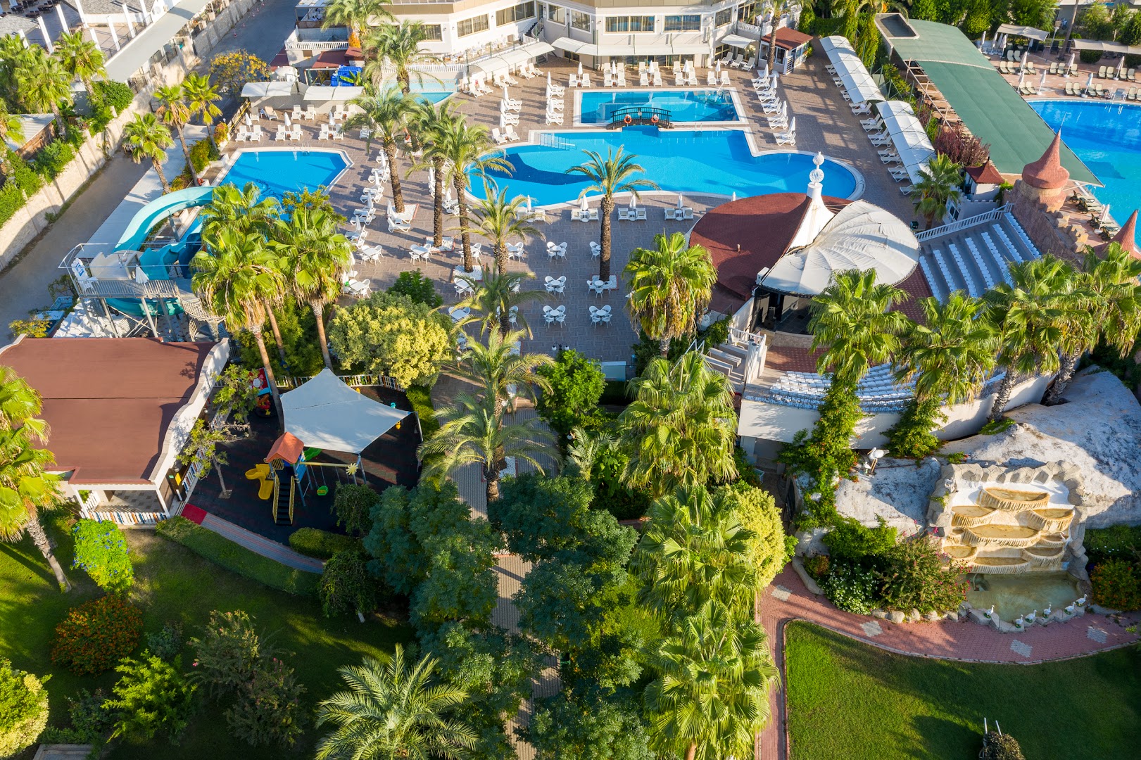 Aydinbey Famous Resort baseinu zona no augšas — vairāki baseini, bērnu slidkalniņi, rotaļu laukums un palmu ieskauta atpūtas zona
