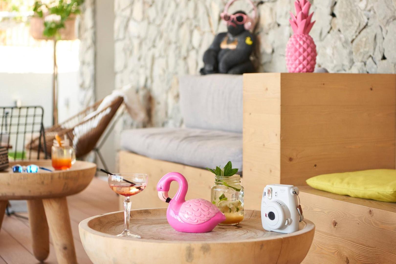 Tuvplāns ar koka galdiņu Moxy Patra Marina terasē, uz kura novietoti kokteiļi, rozā flamingo dekors un tūlītējā foto kamera