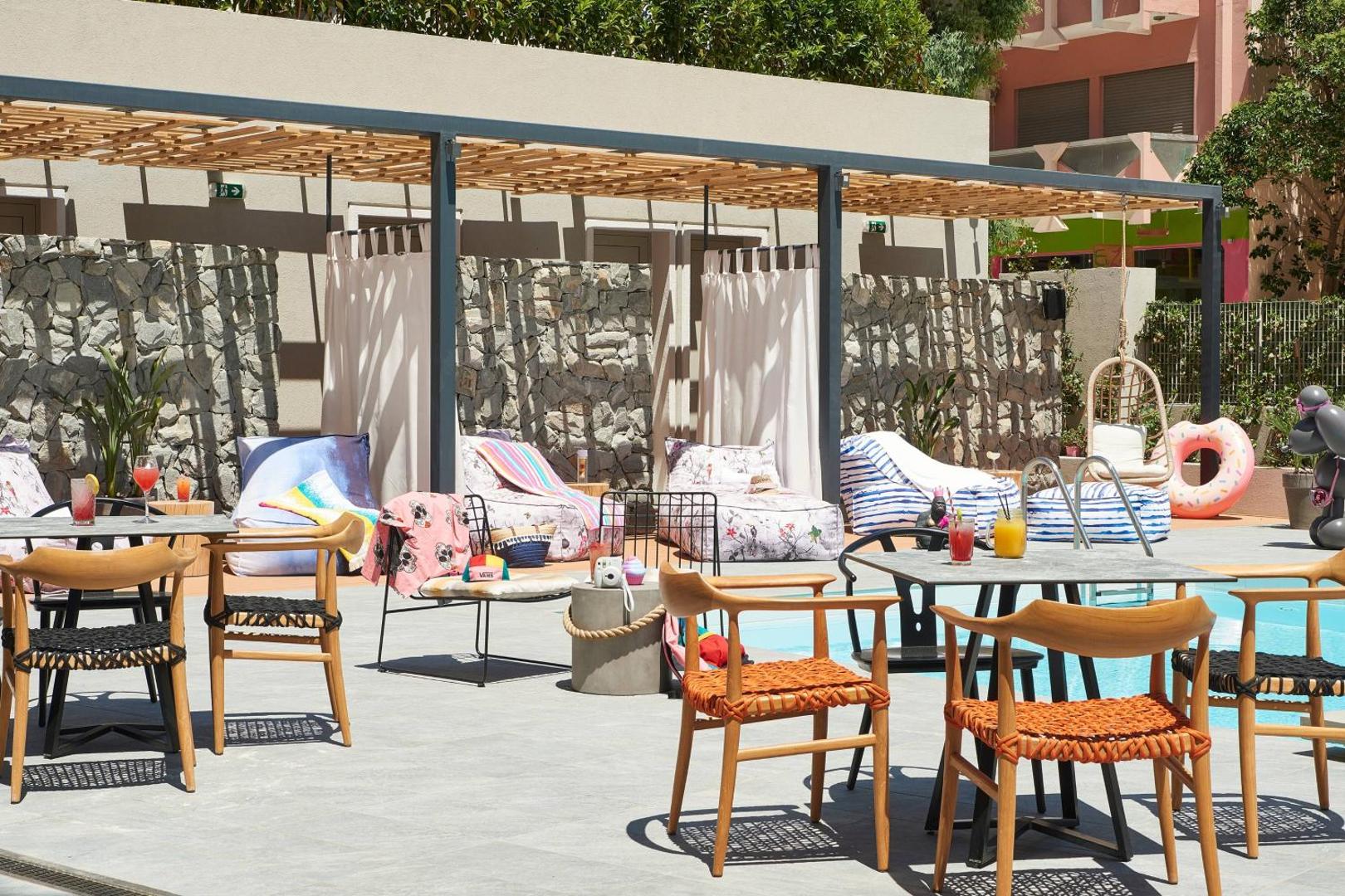 Moxy Patra Marina āra terases bārs un atpūtas zona ar dizaina mēbelēm pie baseina — koka krēsli, galdiņi un koši akcenti