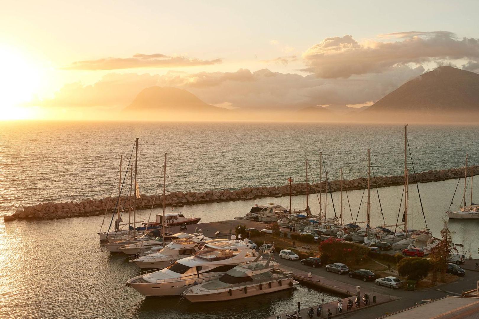 Moxy Patra Marina skats uz jahtu piestātni saulrietā Patras pilsētā Grieķijā — panorāmas skats uz jūru un kalniem zeltītā gaismā