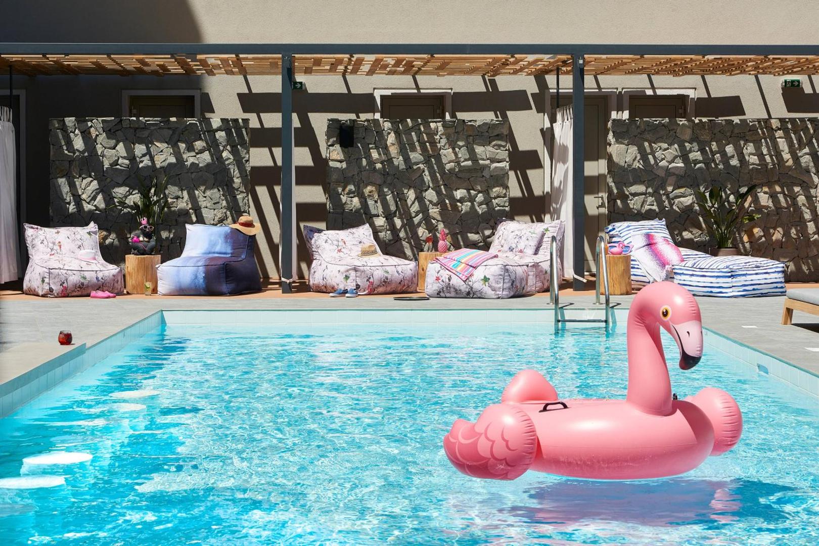 Moxy Patra Marina baseins ar rozā flamingo un atpūtas zonu zem nojumes — akmens sienas dekorācijas un ērti sēžammaisi viesu relaksācijai