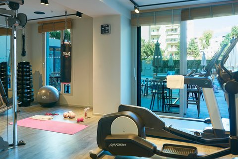 Moxy Patra Marina fitnesa zāle ar moderniem trenažieriem, boksa maisu un skatu caur lielajiem logiem uz āra baseinu
