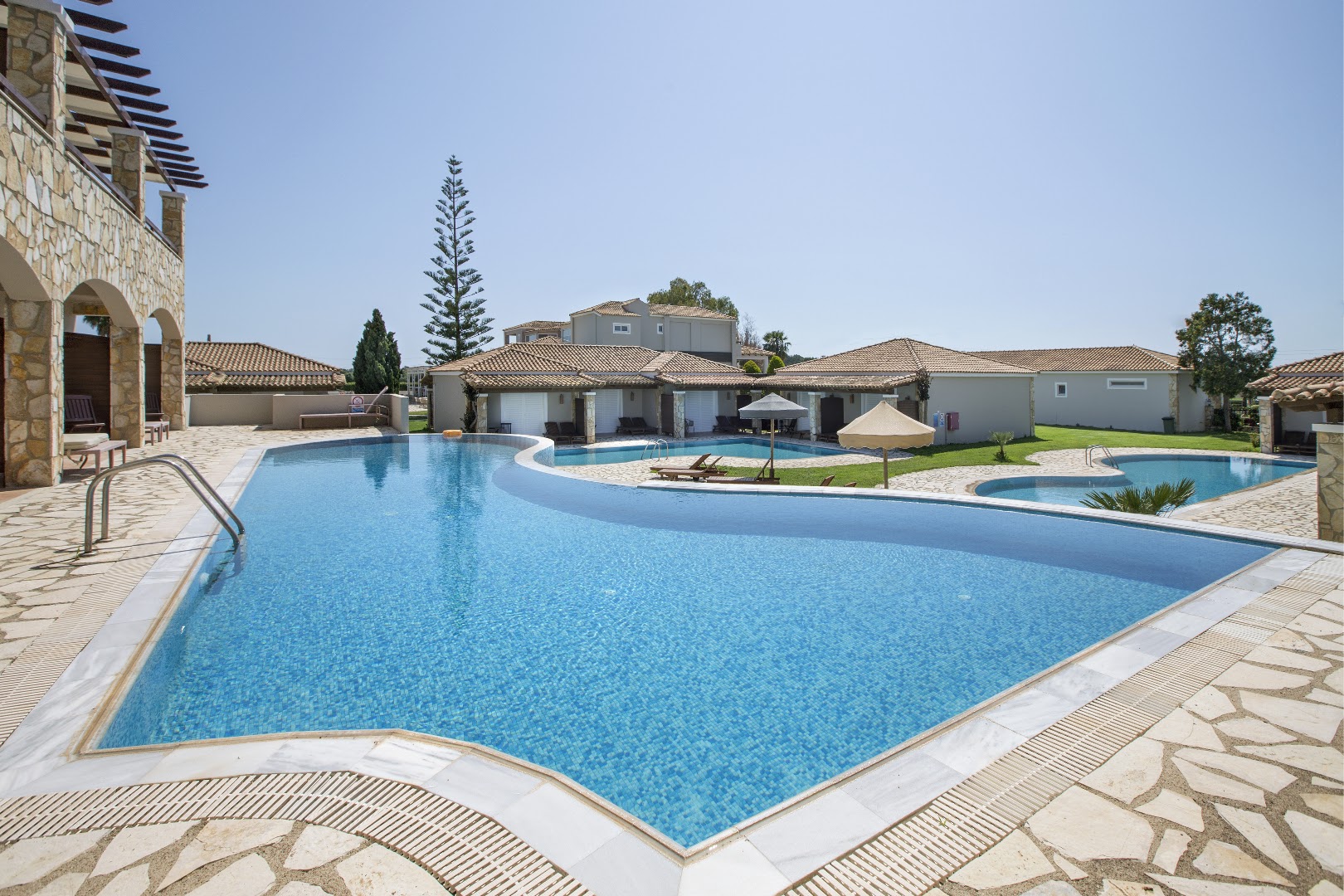 Olympia Golden Beach Resort & Spa galvenais āra baseins ar zilu mozaīkas apdari, apkārtnē bungalo tipa ēkas un akmens terase Peloponēsā