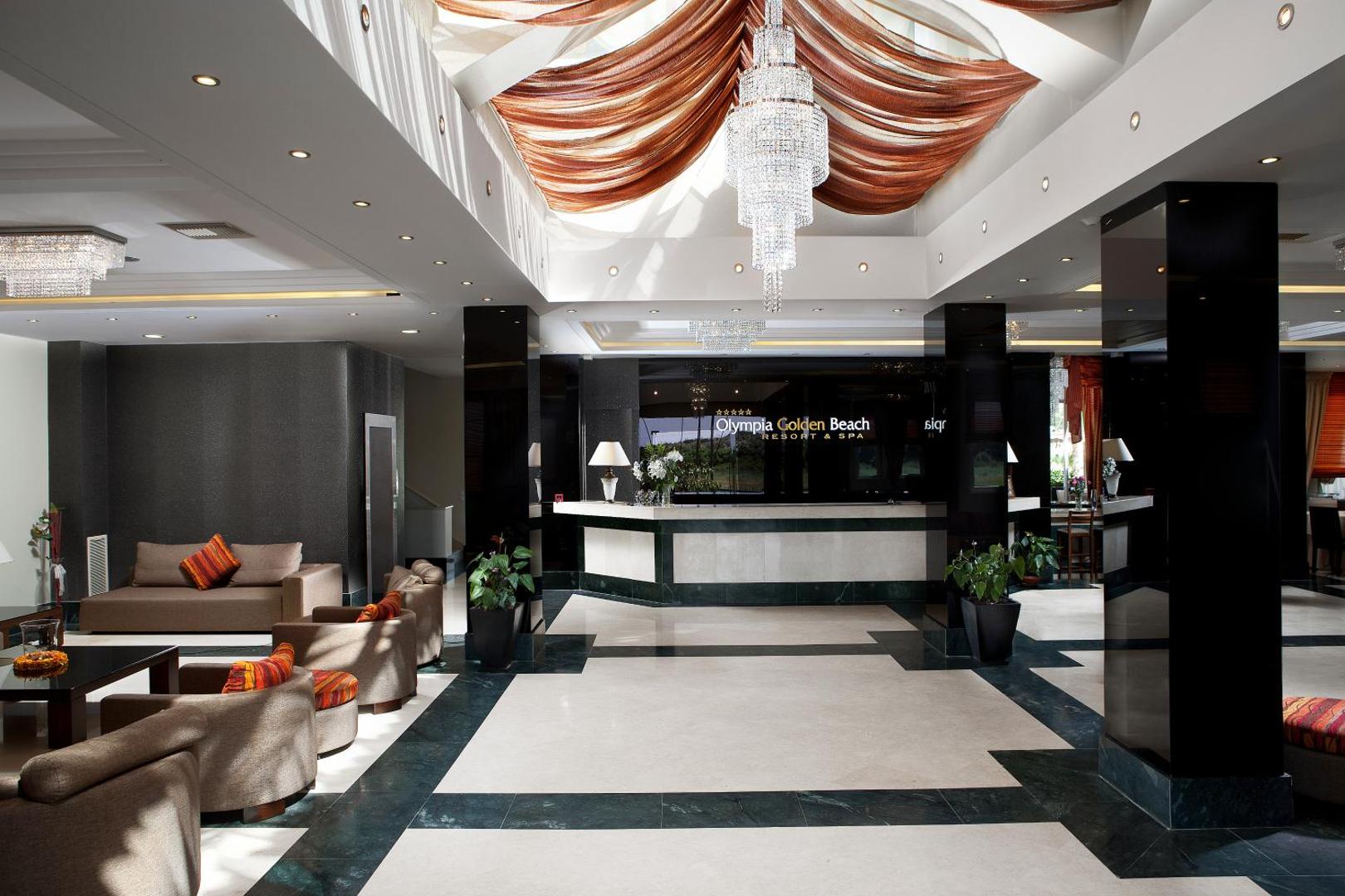 Olympia Golden Beach Resort & Spa grezna lobby zona ar augstiem griestiem, kristāla lustru un marmora grīdu — viesnīcas recepcijas skats
