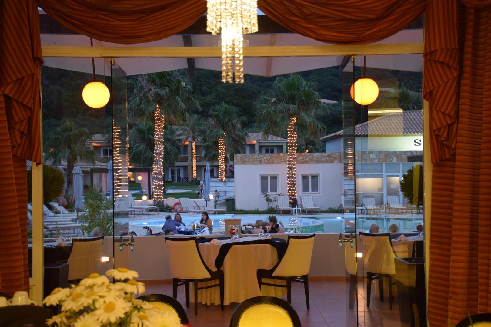 Skats no Olympia Golden Beach Resort & Spa restorāna terases uz izgaismotu baseinu un palmām vakara stundā Peloponēsā.