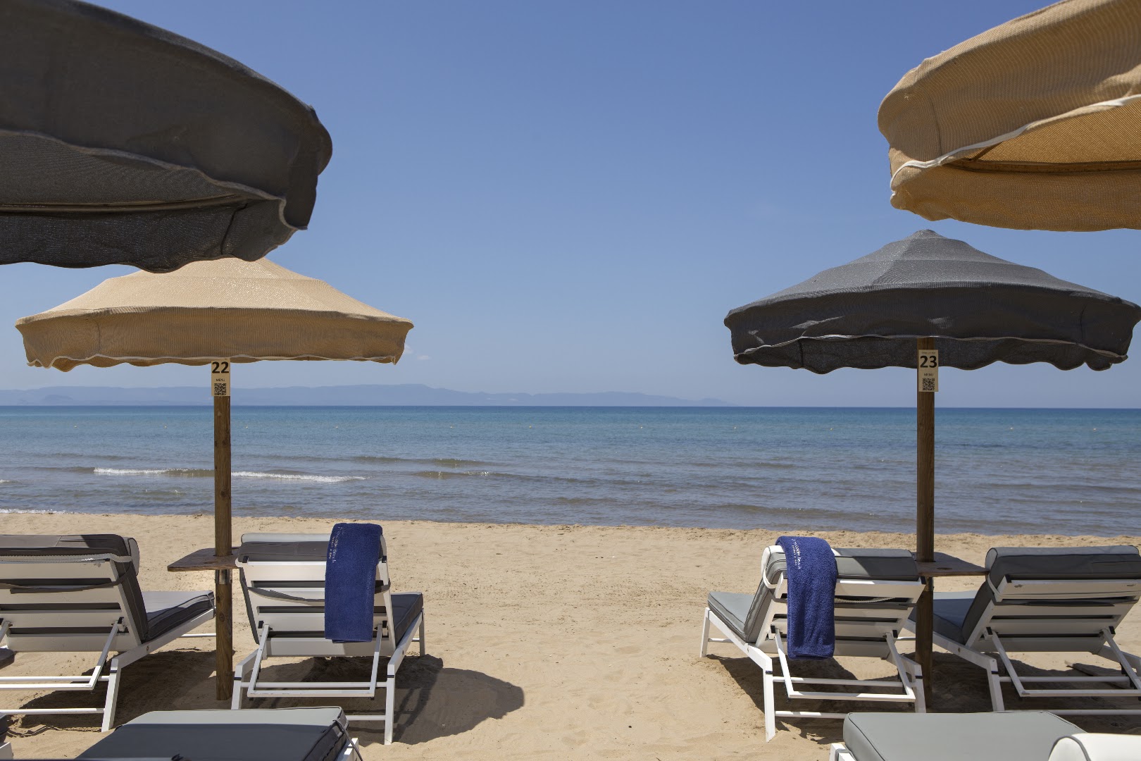 Skats uz Jonijas jūru no Olympia Golden Beach Resort & Spa pludmales zonas ar sakārtotiem sauļošanās krēsliem un saulessargiem.