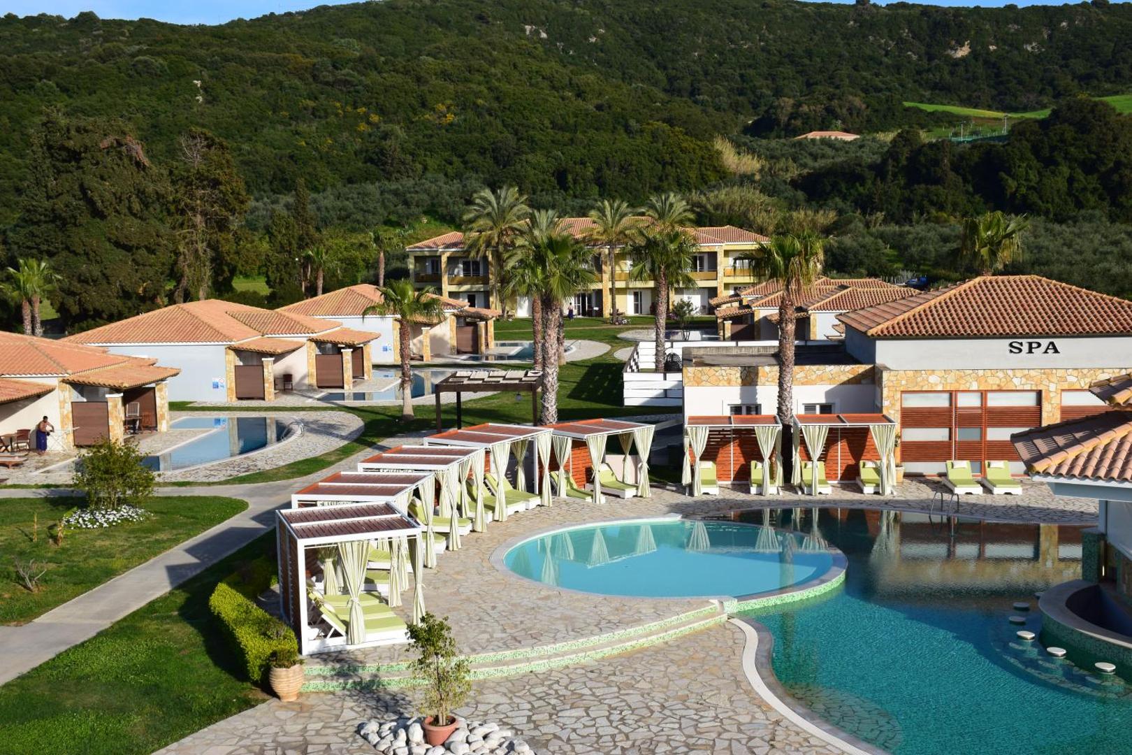 Olympia Golden Beach Resort & Spa galvenais baseins ar atpūtas nojumēm, spa centru un palmu dārzu uz kalnu fona Grieķijā