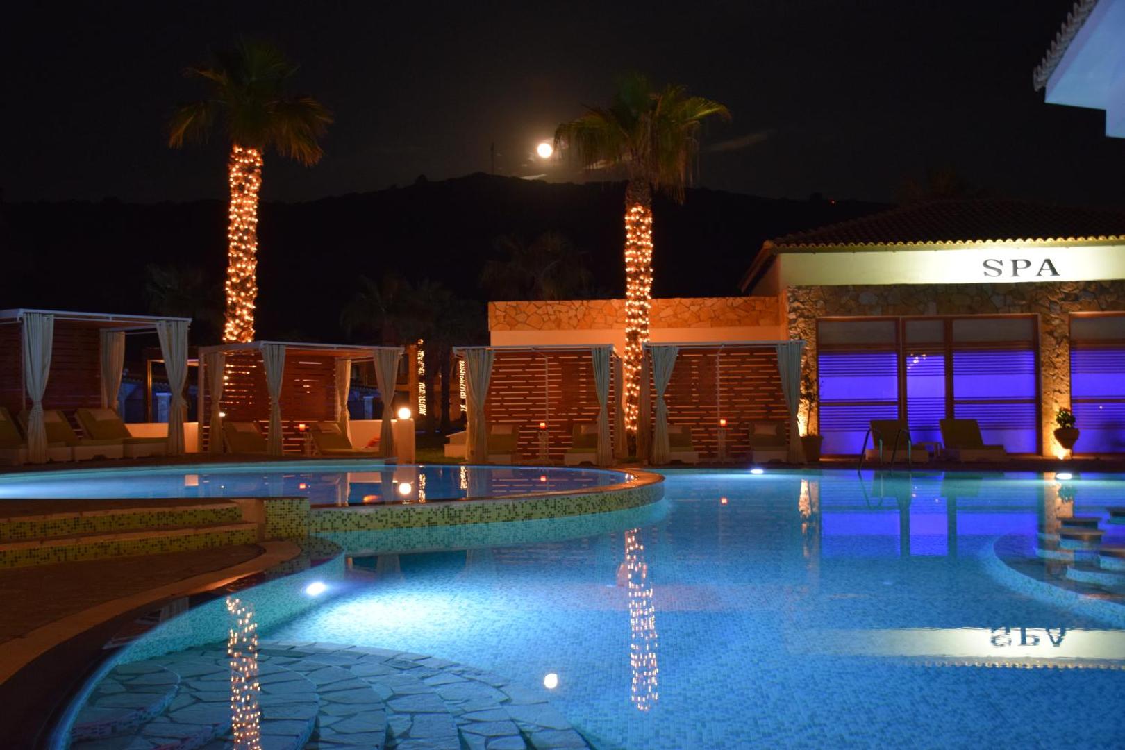 Olympia Golden Beach Resort & Spa izgaismots baseins un spa centrs naktī ar palmām, dekoratīvām gaismām un atpūtas nojumēm