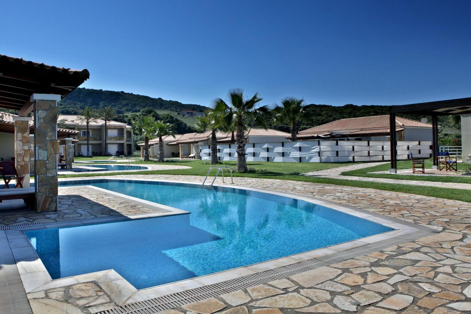 Olympia Golden Beach Resort & Spa koplietošanas baseins pie bungalo rindu mājām ar skatu uz zaļiem pakalniem un palmām