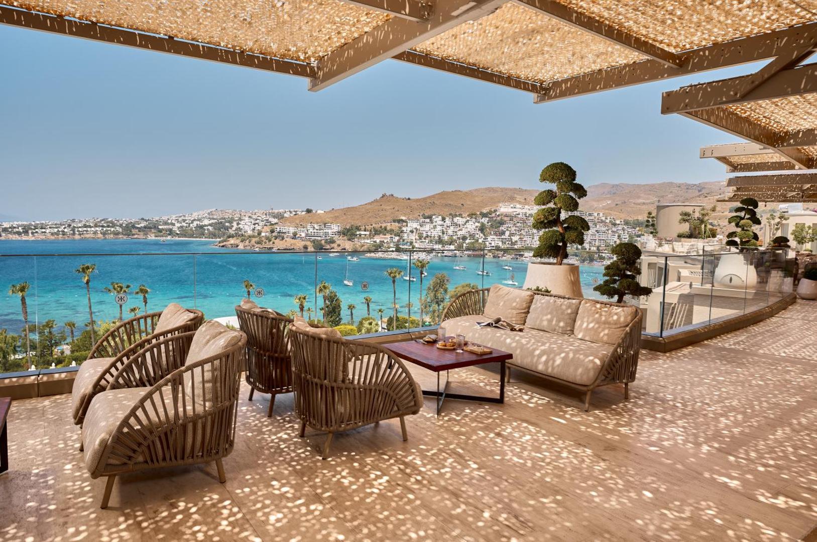 Kefaluka Resort Hotel āra terase ar mīkstajām mēbelēm un panorāmas skatu uz līci un Bodrumas piekrastes kalniem