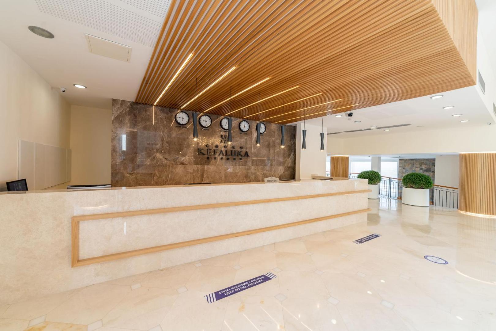 Kefaluka Resort Hotel viesnīcas recepcija ar marmora apdari, koka griestu elementiem un pasaules pulksteņiem pie sienas