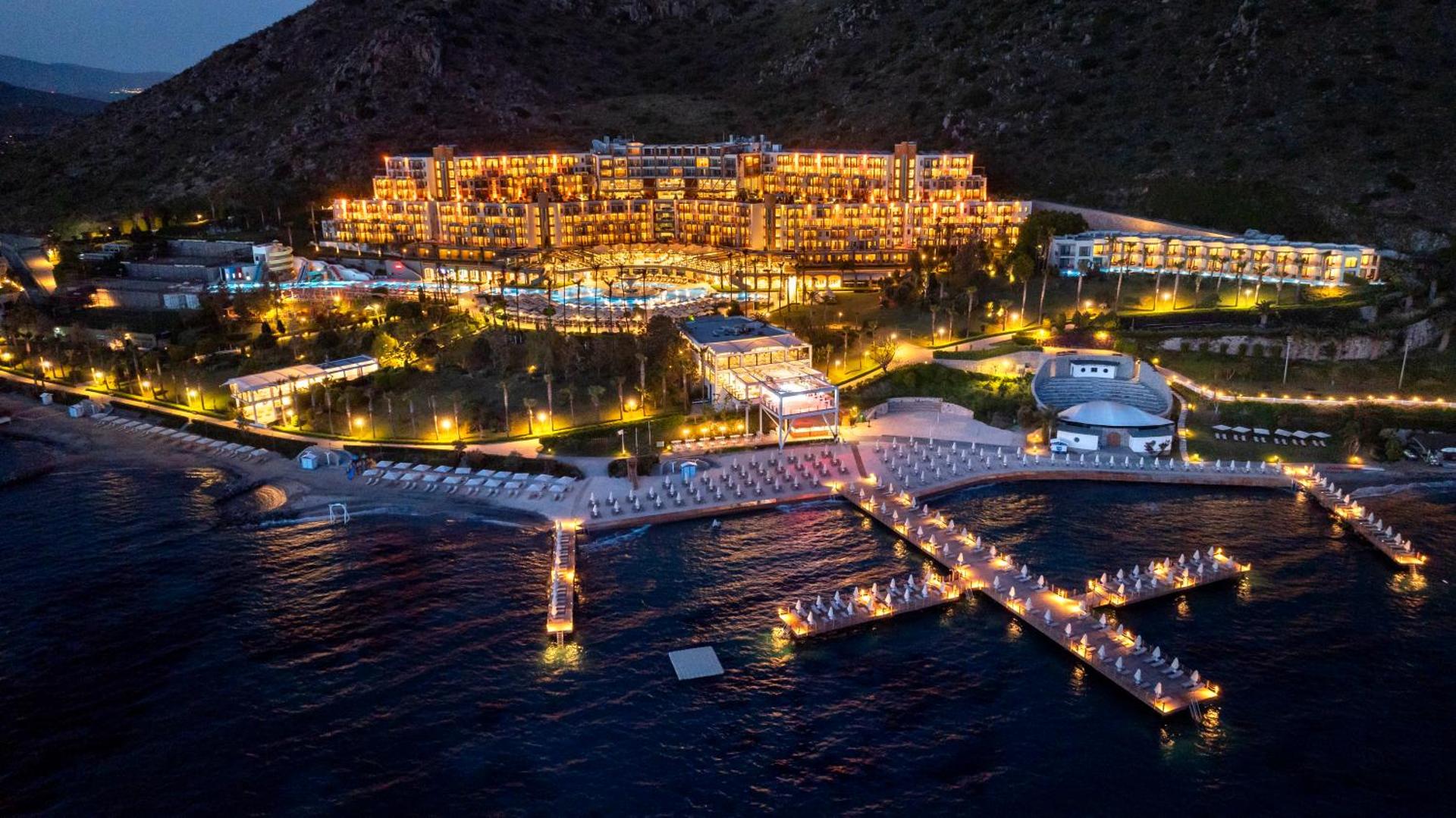Kefaluka Resort Hotel nakts skats ar izgaismotām piestātnēm un galveno ēku — luksusa kūrorts Bodrumā pie Egejas jūras naktī