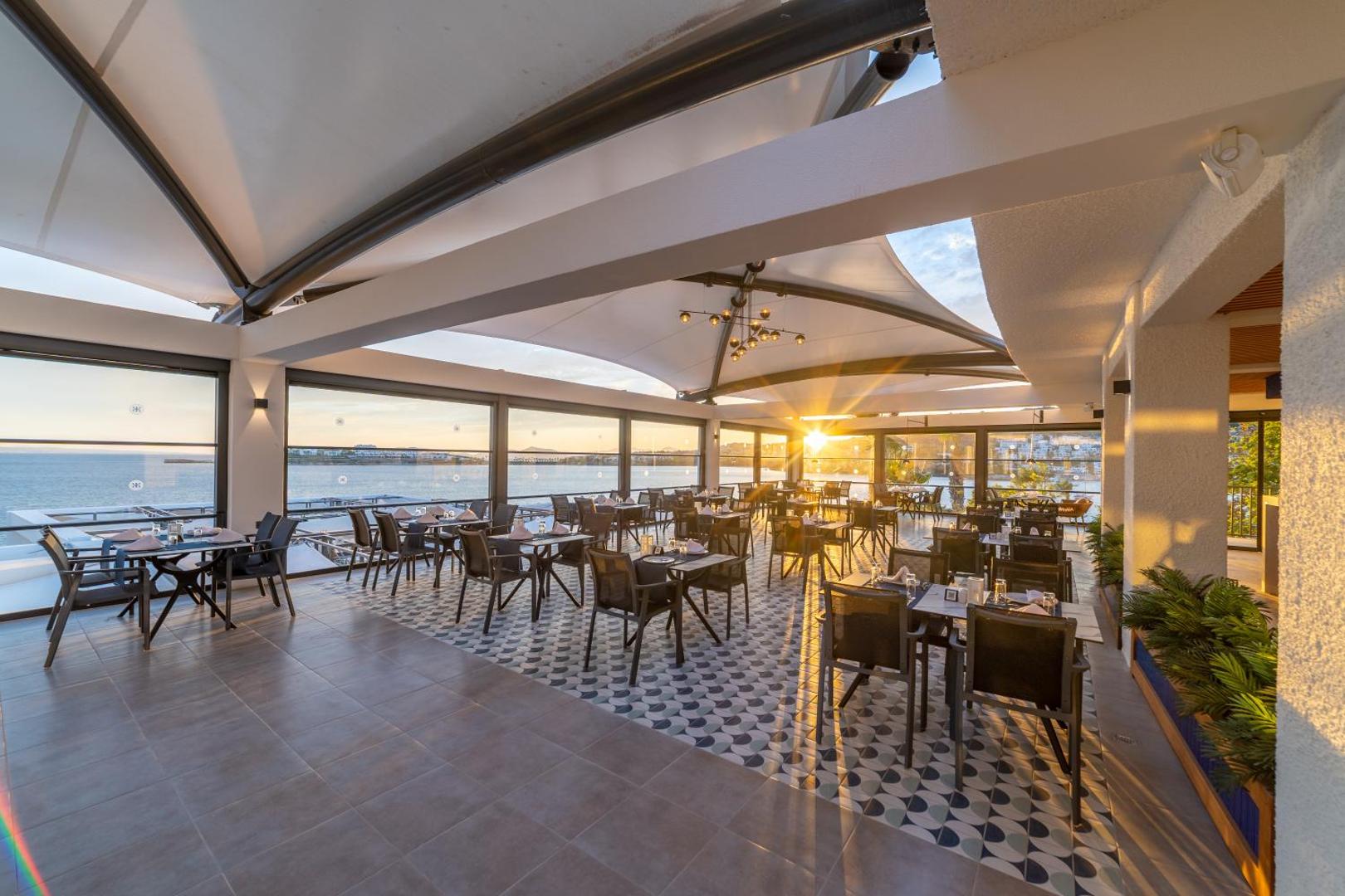 Kefaluka Resort Hotel restorāna terase saulrietā ar skatu uz jūru Bodrumā — eleganti klāti galdi un panorāmas logi