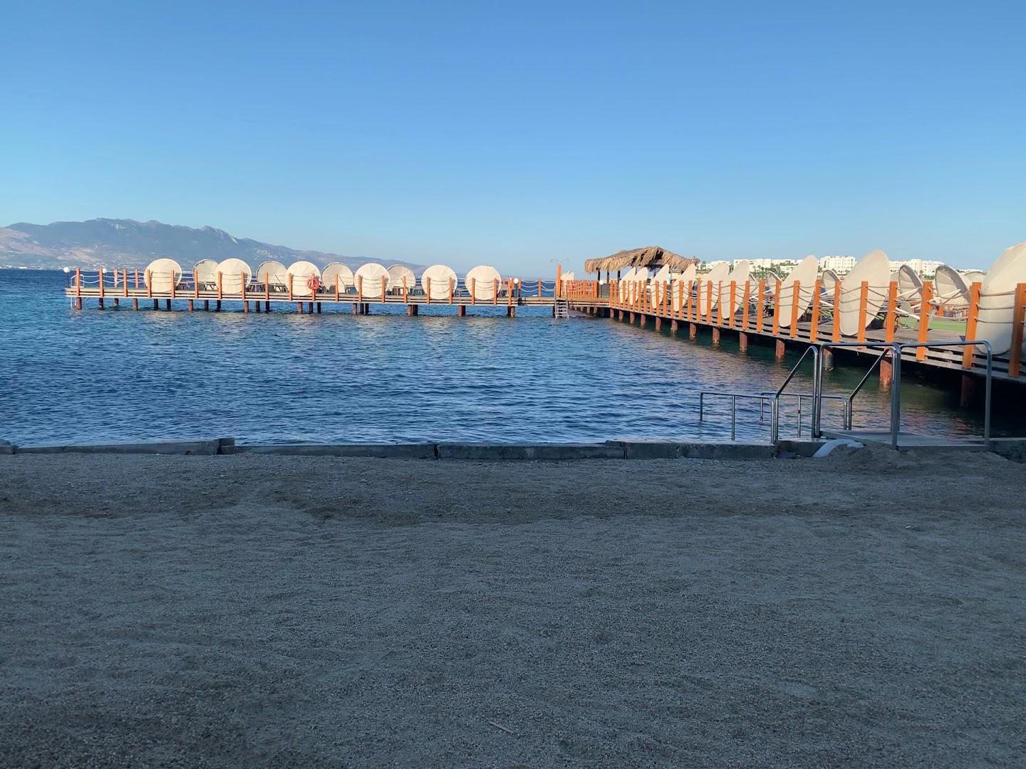 Kefaluka Resort koka piestātne ar modernām atpūtas nojumēm un skatu uz kalniem Bodrumā — mierīga jūra rīta gaismā