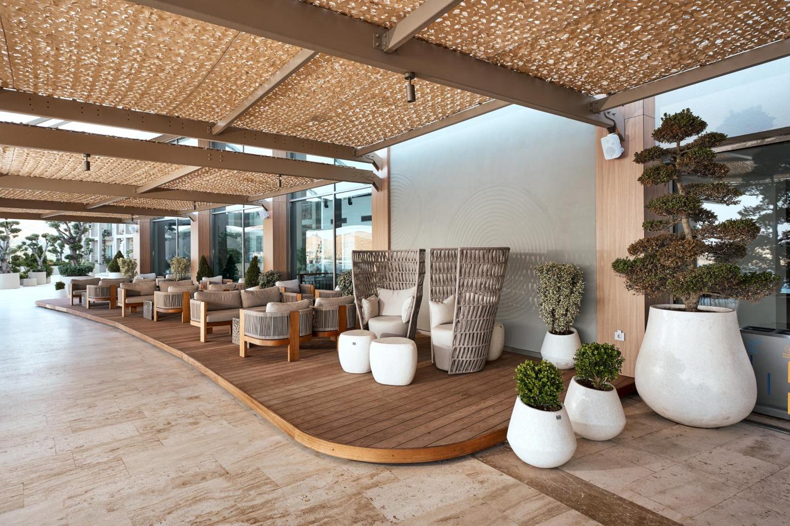 Kefaluka Resort āra terase ar modernām pītām mēbelēm, koka klāju un dekoratīviem augiem podos atpūtai piekrastē