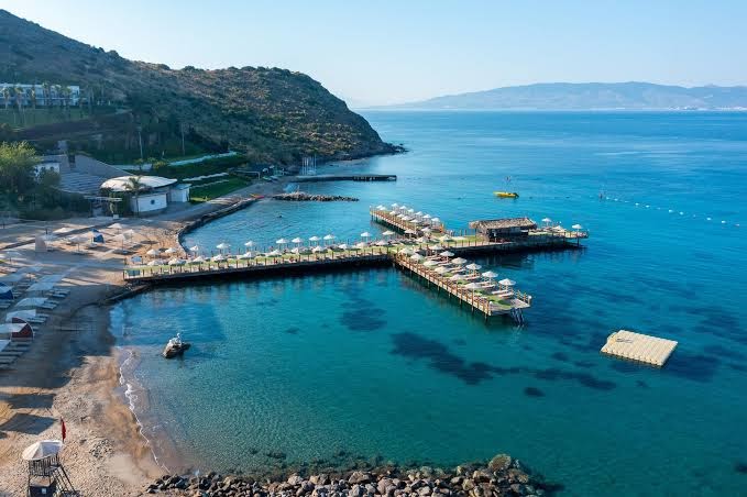 Kefaluka Resort aerofoto skats uz tirkīzzilo līci un koka piestātnēm Bodrumā — kristāldzidrs ūdens un piekrastes reljefs