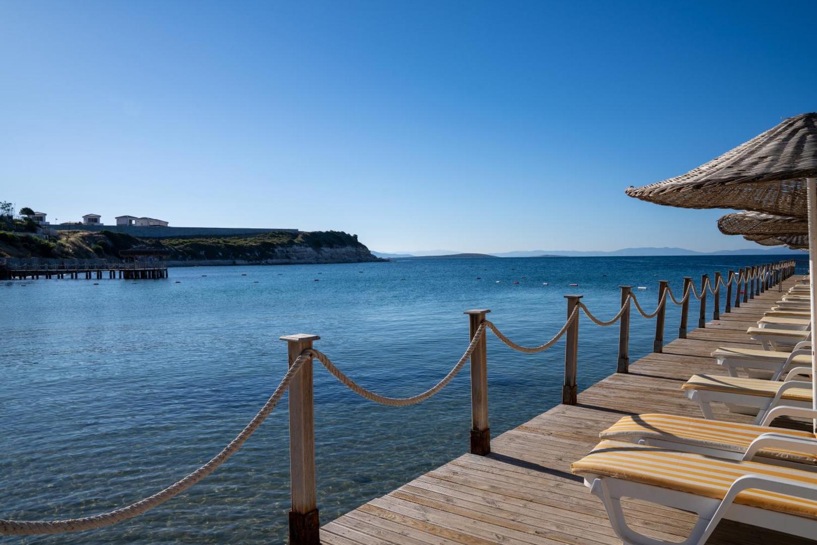 Skats no Anadolu Hotels Didim Club koka laipas uz mierīgo jūras līci un piekrastes ainavu saulainā dienā