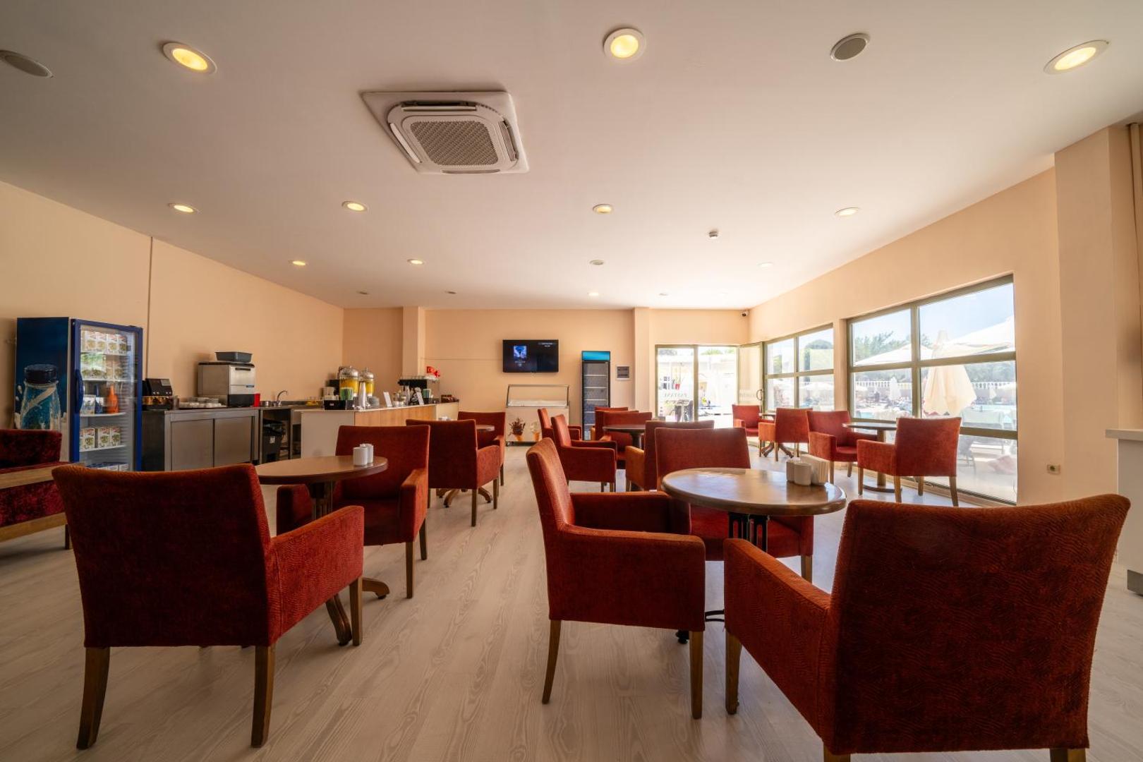 Anadolu Hotels Didim Club viesnīcas bārs un atpūtas zona ar sarkaniem krēsliem un gaišu interjeru