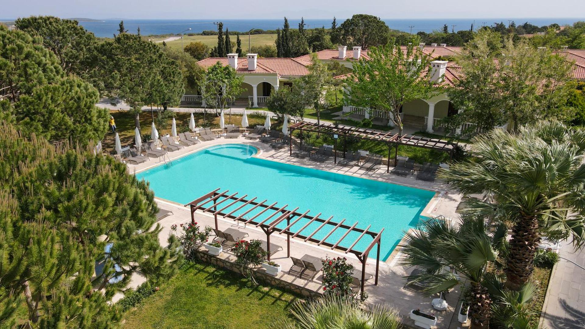 Anadolu Hotels Didim Club klusais baseins dārza zonā pie bungalo numuriem, ko ieskauj priedes, palmas un labiekārtota sauļošanās terase.