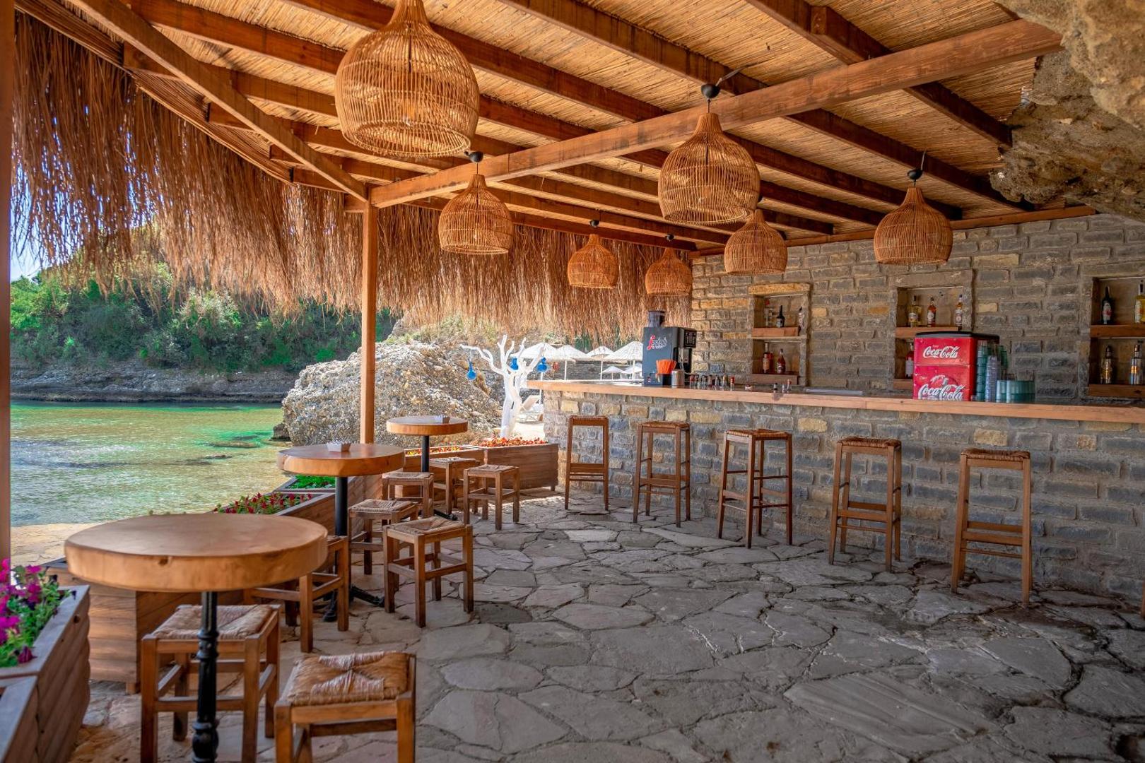 Utopia Beach Club pludmales bārs ar salmu jumtu, akmens sienām un skatu uz tirkīza krāsas līci