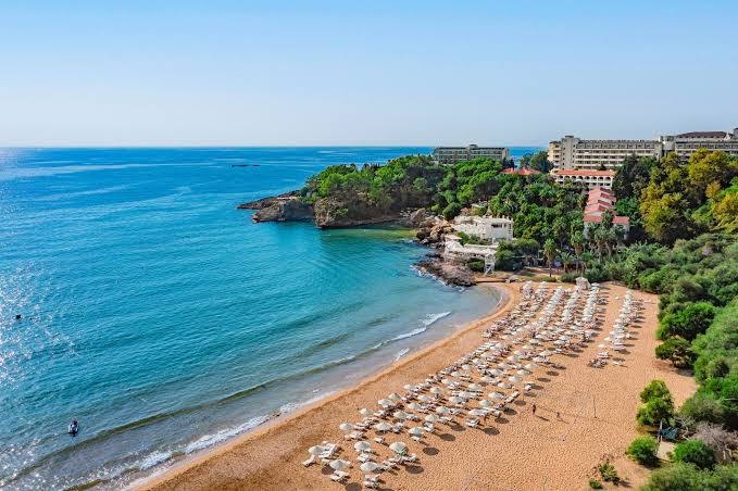Utopia Beach Club viesnīcas teritorija no putna lidojuma — plaša smilšu pludmale ar saulessargiem, zaļi meži un Vidusjūras piekraste