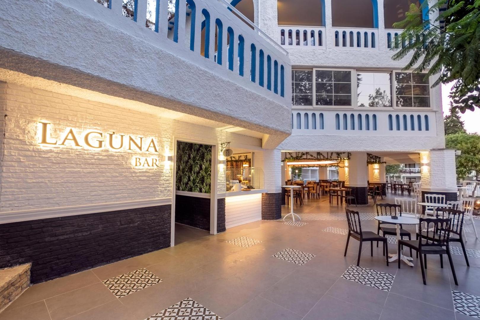 Viesnīcas Utopia Beach Club Laguna bāra terase vakarā ar galdiņiem un izgaismotu ēkas fasādi