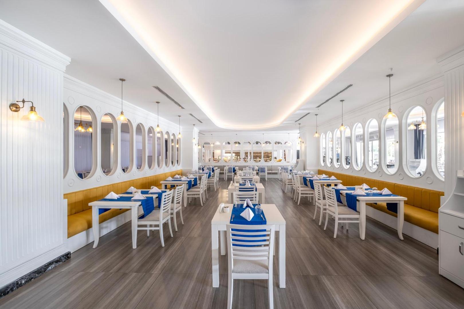 Utopia Beach Club iekštelpu restorāns ar modernu dizainu, baltām mēbelēm, ziliem akcentiem un dekoratīviem spoguļiem pie sienām