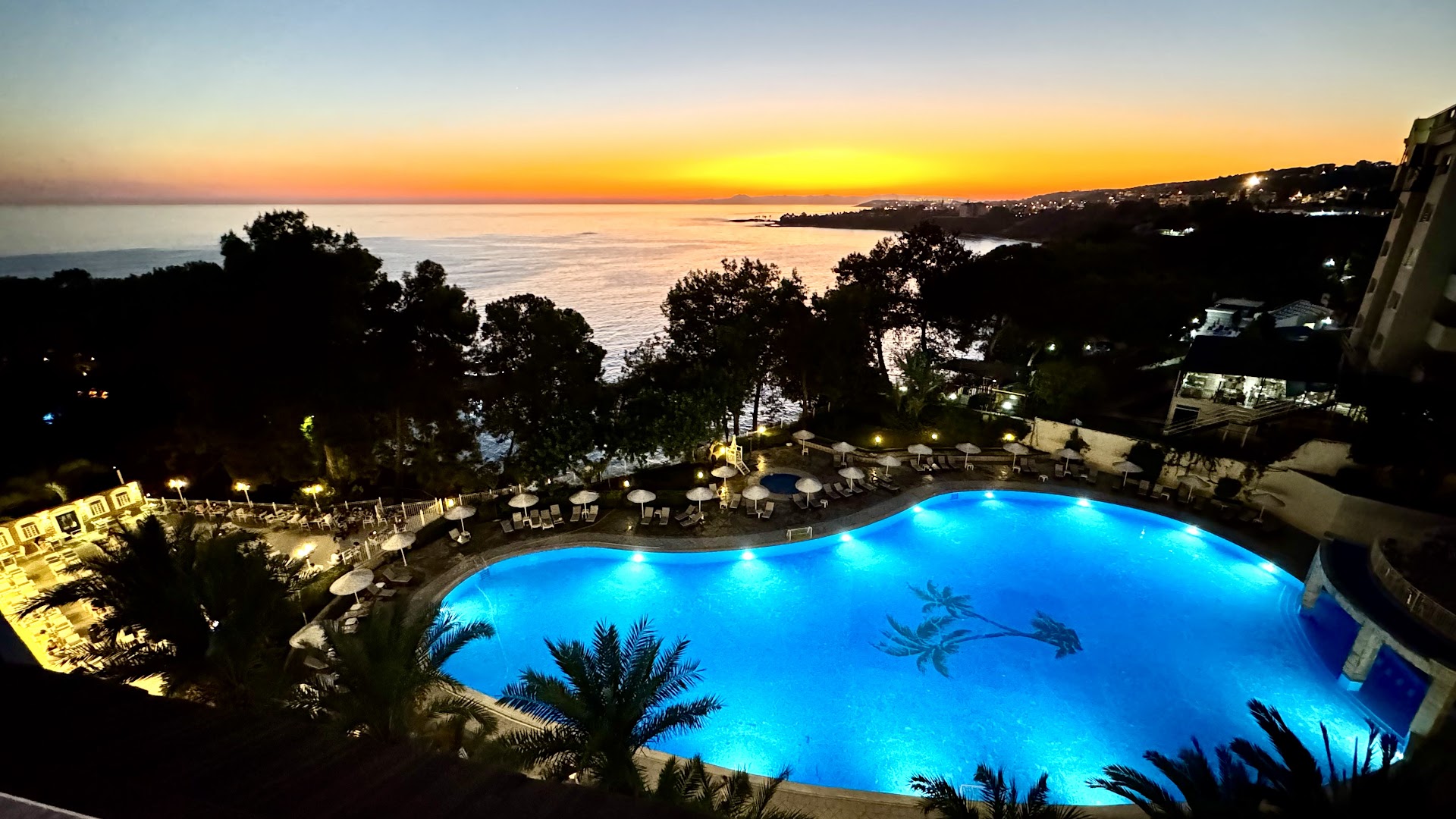 Utopia Beach Club baseins vakarā ar apgaismojumu un saulrietu virs Vidusjūras Alānijas piekrastē — romantiska atmosfēra un palmu silueti