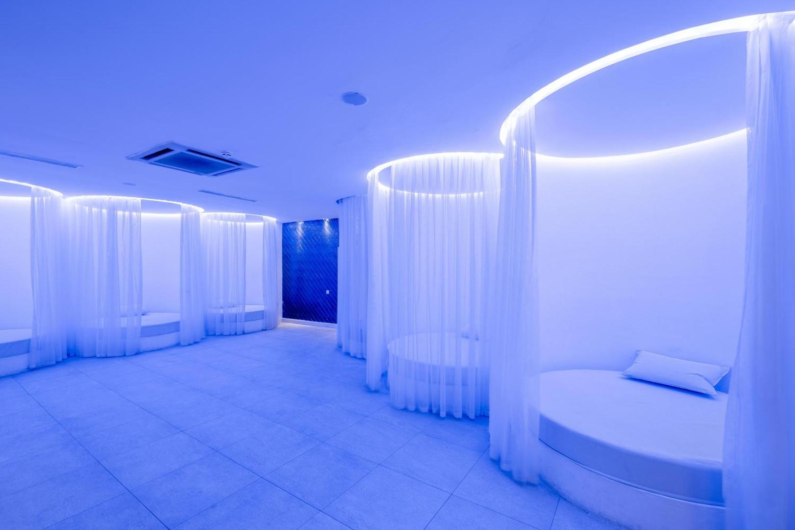 Utopia Beach Club moderna atpūtas telpa ar zilu apgaismojumu un apaļām gultām, ko ieskauj balti aizkari