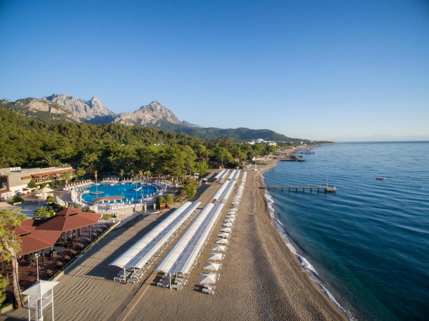 Kimeros Park Holiday Village panorāmas skats uz plašo smilšu pludmali, āra baseinu un apkārtējiem kalniem Kemeras reģionā, Turcijā