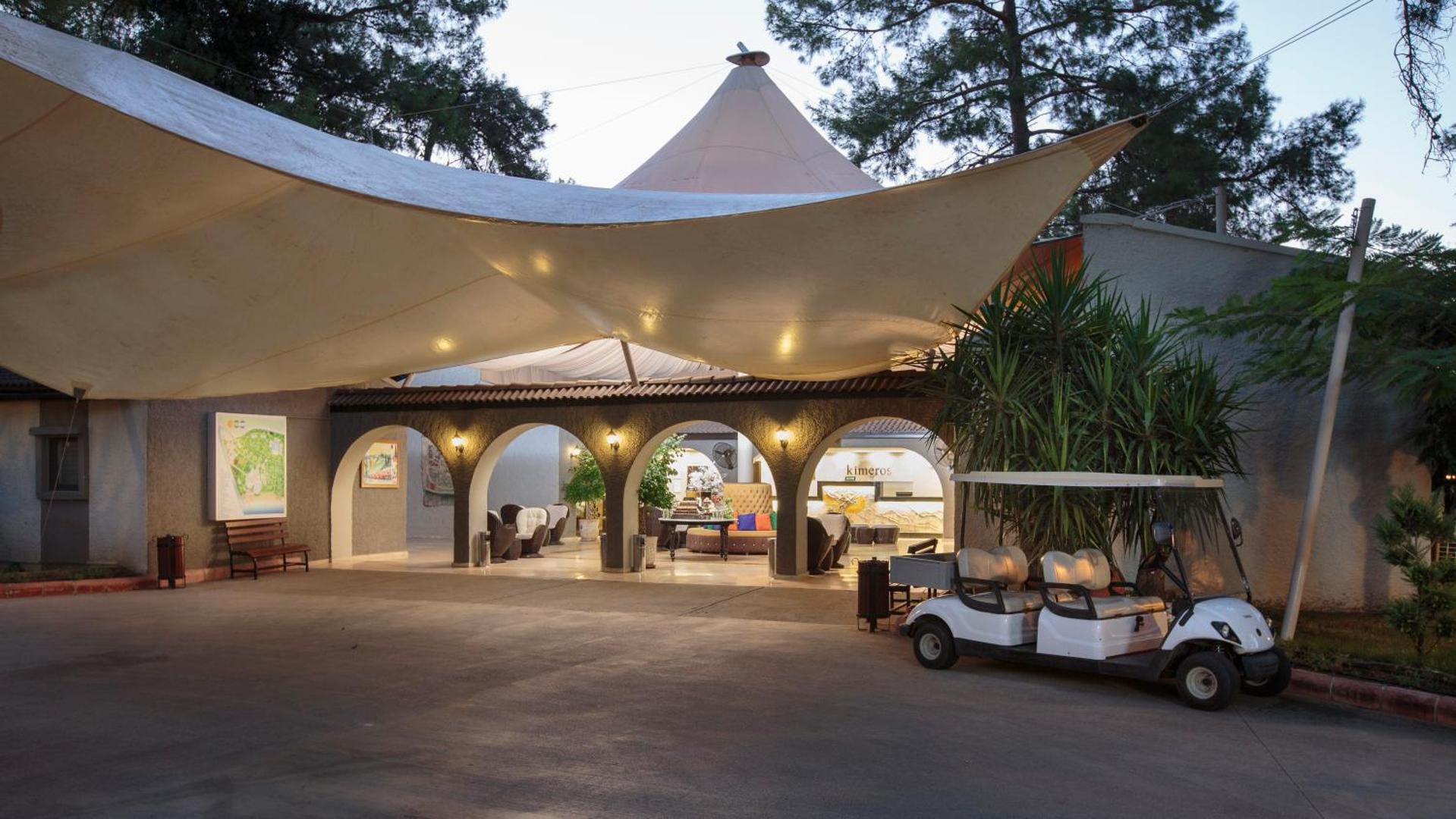 Kimeros Park Holiday Village viesnīcas ieeja un lobby zona vakarā ar dekoratīvu tentu un golfa mašīnīti.