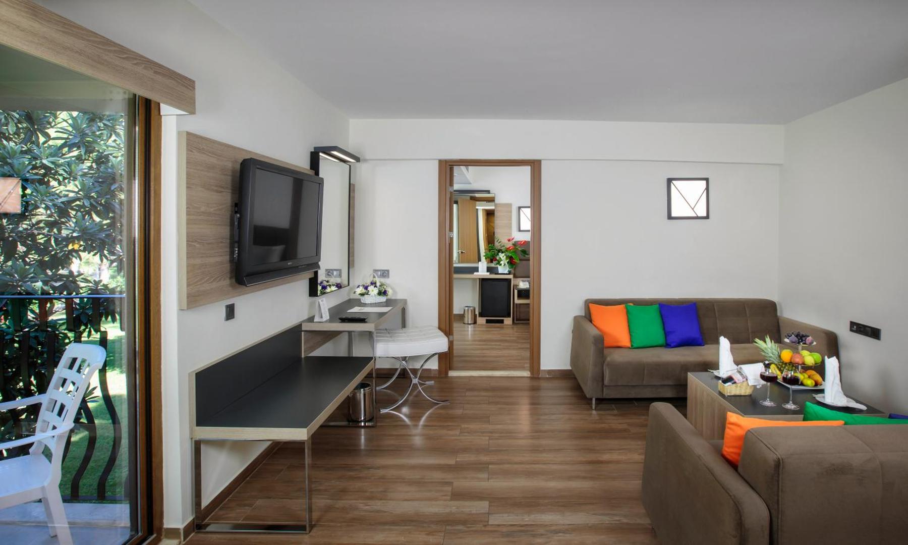 Kimeros Park Holiday Village ģimenes numura viesistaba ar dīvāniem, krāsainiem spilveniem, televizoru un izeju uz balkonu dārza pusē