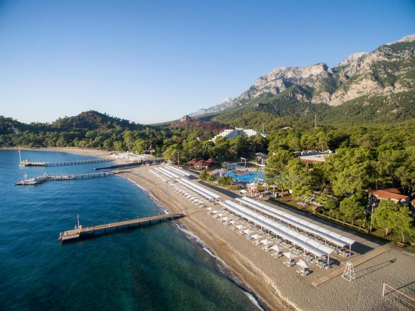 Kimeros Park Holiday Village privātā pludmale ar koka piestātnēm, saulessargiem un dzidru Vidusjūras ūdeni Kemeras piekrastē, Turcijā.