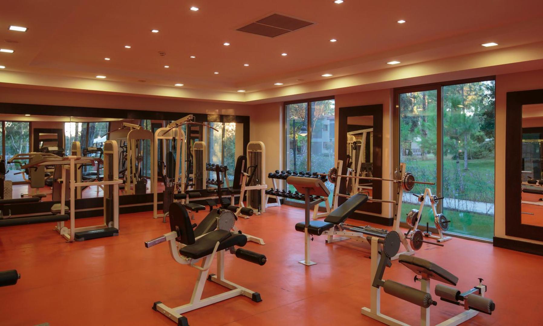 Kimeros Park Holiday Village moderns fitness centrs ar trenažieriem un skatu caur lielajiem logiem uz viesnīcas dārzu