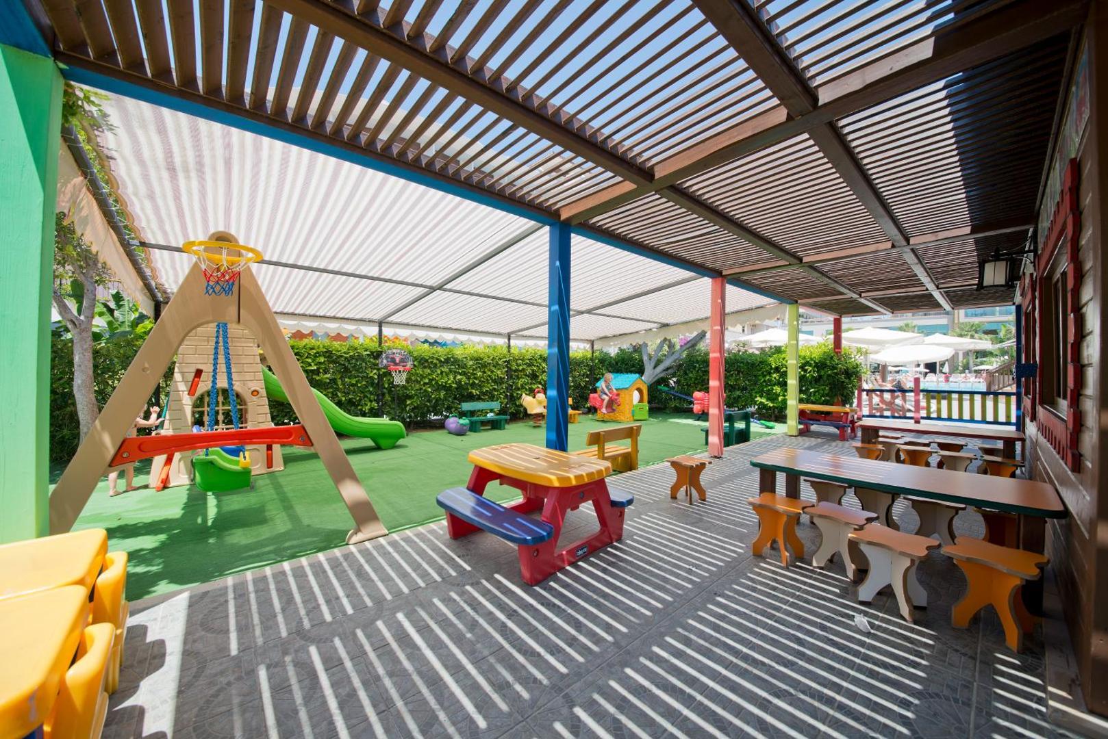 Aydinbey Kings Palace bērnu rotaļu laukums zem nojumes ar slidkalniņiem un galdiņiem radošām nodarbībām Sides kūrortā, Turcijā