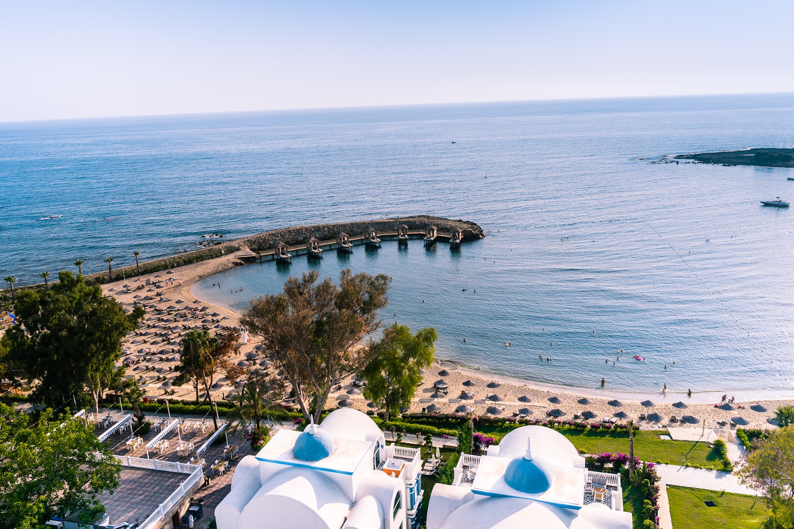 Rubi Platinum SPA Resort & Suites privātā pludmale ar līci, saulessargiem un koka piestātni ar atpūtas namiņiem Alanjā