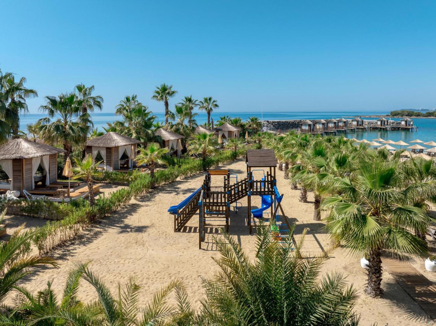 Rubi Platinum SPA Resort & Suites bērnu rotaļu laukums smilšainā pludmalē ar palmām un bungalo pie jūras