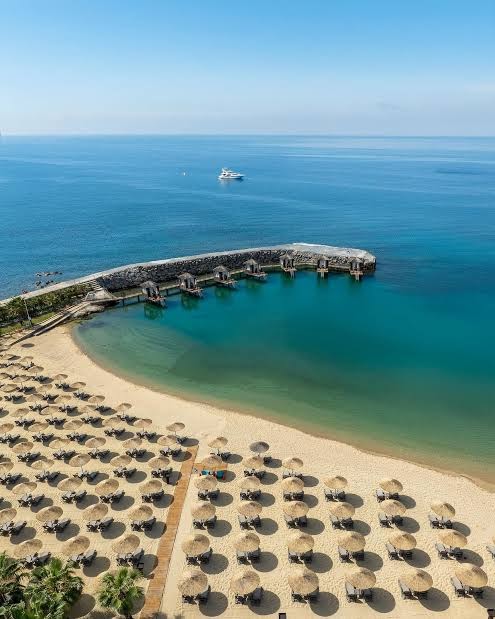 Rubi Platinum SPA Resort & Suites pludmales zona ar daudziem saulessargiem un atpūtas krēsliem pie tirkīzzila līča Alānijā