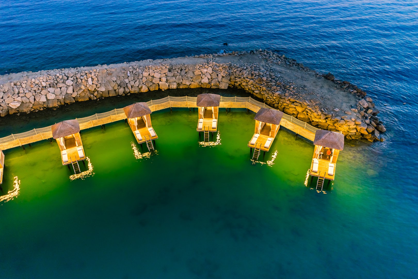 Rubi Platinum SPA Resort & Suites bungalo izgaismojums vakarā virs jūras līča Alānijā — vakara atmosfēra un koka laipas
