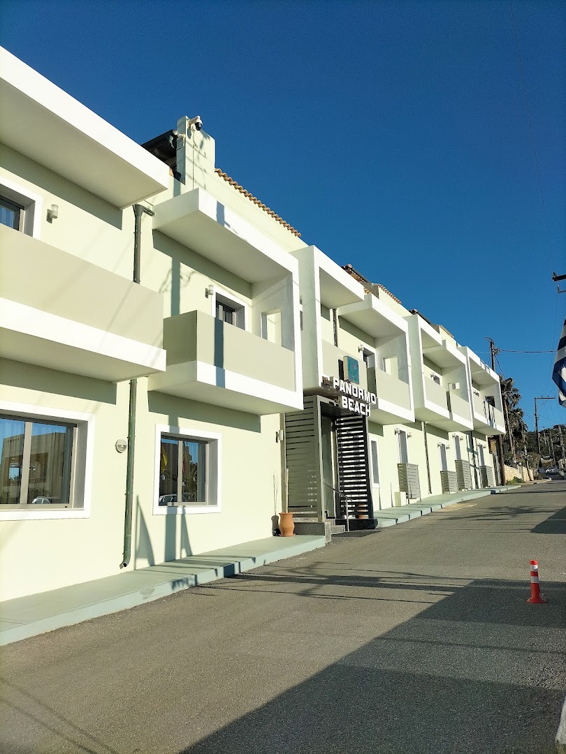 Panormo Beach viesnīcas ēka no ielas puses — moderna arhitektūra ar gaišiem balkoniem un ieeju Panormo ciematā