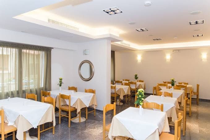Panormo Beach restorāna iekštelpas ar klasiski klātiem galdiem, baltiem galdautiem un dekoratīviem ziediem