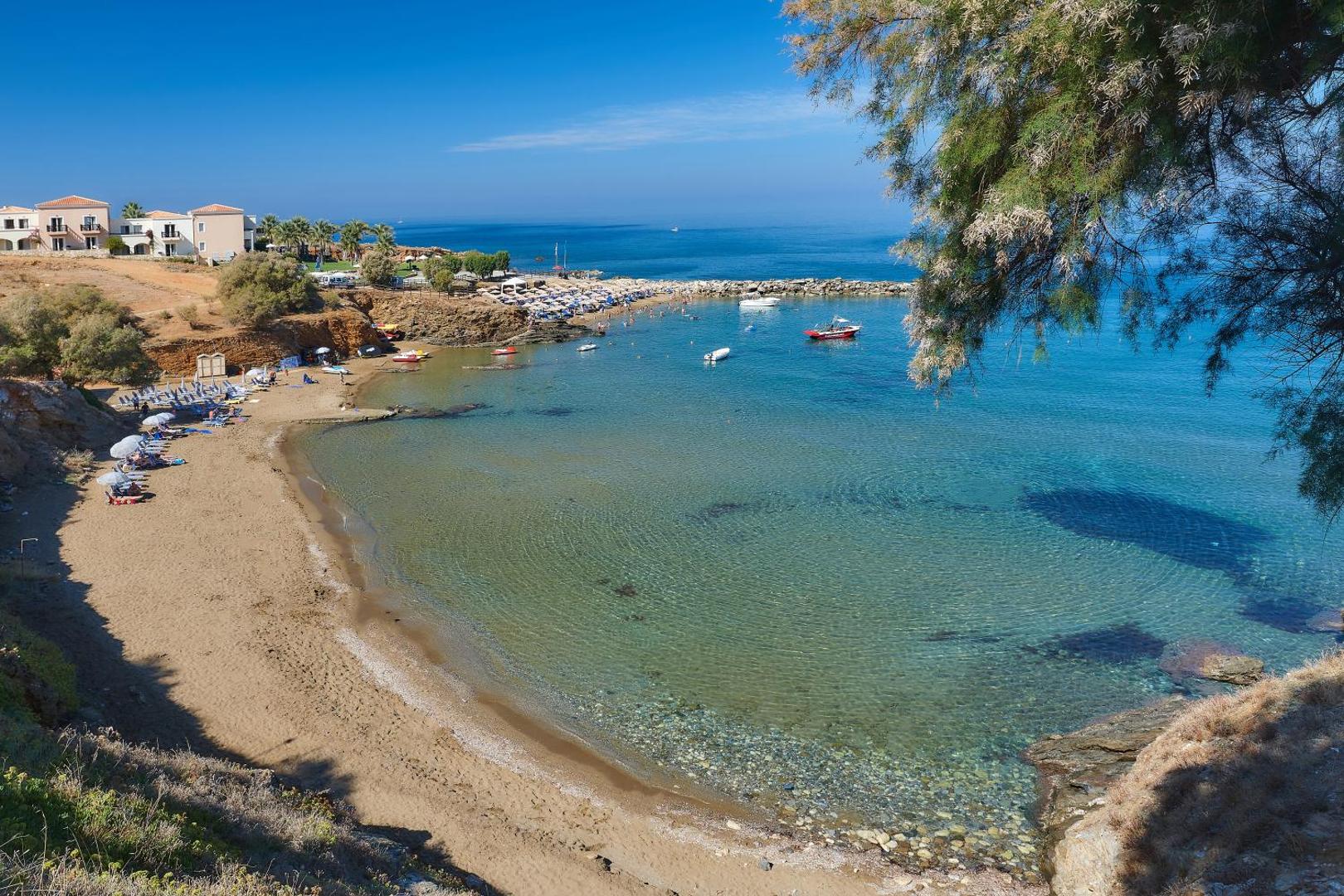 Panormo Beach panorāmas skats uz smilšu pludmali, dzidro jūras līci un piekrastes klintīm saulainā dienā Krētā