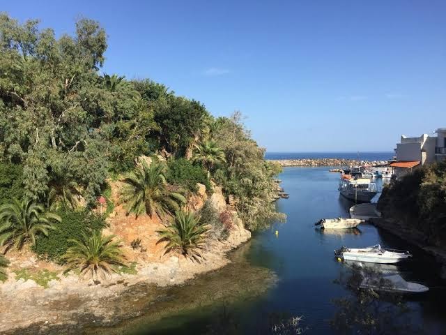 Skats uz Sisi ciemata ostu un piekrasti netālu no Koutrakis Suites by Estia — palmas, klintis un nelielas laivas līcī.