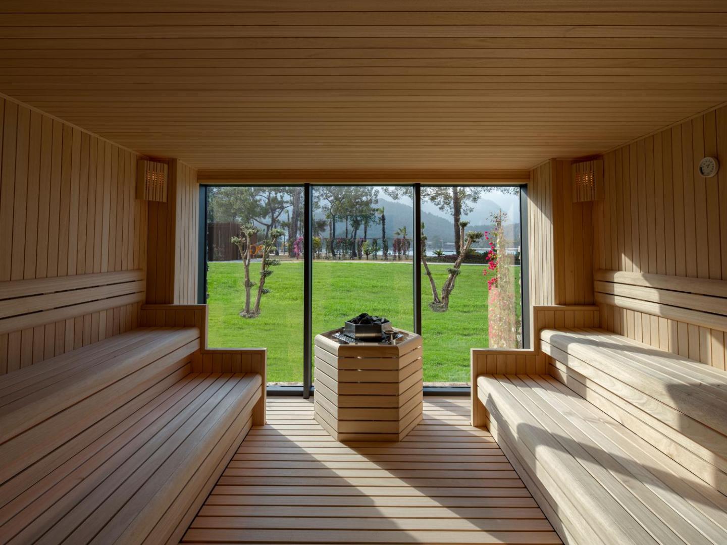 NG Phaselis Bay viesnīcas sauna ar panorāmas logu uz dārzu Kemeras reģionā — koka apdare un skats uz zaļo zonu